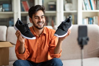 Yakışıklı, sakallı, genç, orta doğulu bir moda blogcusu takipçilerine yeni ayakkabılarını gösteriyor. Siyah şık koşu ayakkabıları, evdeki koltukta oturuyor, akıllı telefondan yayın yapıyor, paketleri açıyor.