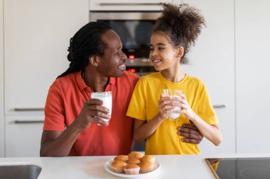 Tatlı siyah prematüre kız ve babası mutfakta abur cubur yiyor, mutlu Afrika kökenli Amerikalı baba ve masa başında oturan ve ev yapımı, sütlü kek yiyen, bedava yer alan kız çocuğu.