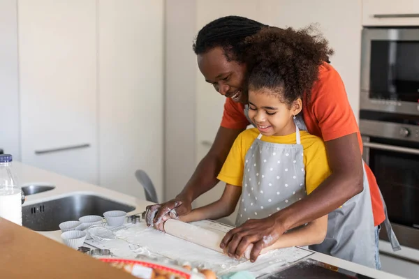 Loving Black Dad Teaching His Preteen Daughter How To Roll Dough While Baking Together At Home, African American Father And Female Child Using Roller Pin While Cooking Pastry In Kitchen, Copy Space