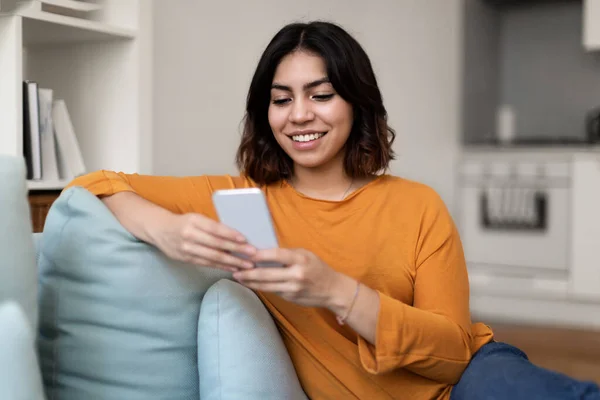 Mujer Árabe Sonriente Usando Smartphone Mientras Relaja Sofá Casa Hermosa —  Fotos de Stock