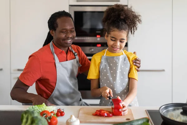 Happy African American Dad And Daughter Cooking Together In Kitchen Interior, Cheerful Black Father And Female Child Enjoying Preparing Healthy Food At Home, Making Fresh Vegetable Salad, Free Space