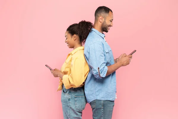 人々と技術の概念 陽気な正の黒のカップルのプロフィールショットに戻るに立って 保持し 彼らの携帯電話を使用して オンラインでチャット バナー サイドビュー — ストック写真