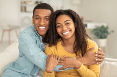 Gülümseyen bin yıllık Afro-Amerikan erkeği kadınlara sarılıyor, romantizmden, aşktan, boş zamanlardan ve aydınlık oturma odasında kameraya bakmaktan zevk alıyor. Video çağrısı, harika haberler, ruh hali ve evde aile ilişkisi.