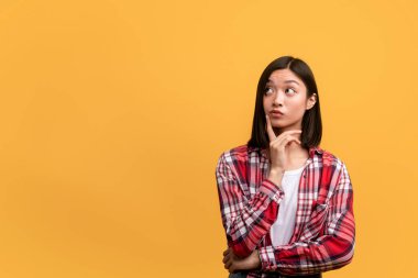 Bir düşüneyim. Fotokopi odasına bakan düşünceli Asyalı kadın, teklif ya da anlaşma hakkında düşünüyor ve çeneye dokunuyor, sarı stüdyo arka planında duruyor, afiş.