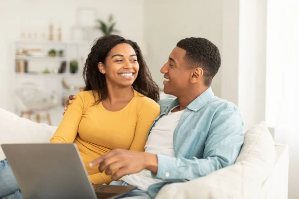 何百万人ものアフリカ系アメリカ人の男性が女性を見て笑っているオンライン通話のためにラップトップを使用し 光のリビングルームのインテリアでビデオを見てください インターネットでサーフィン 素晴らしいニュース ロマンチックで家で人々の感情 — ストック写真
