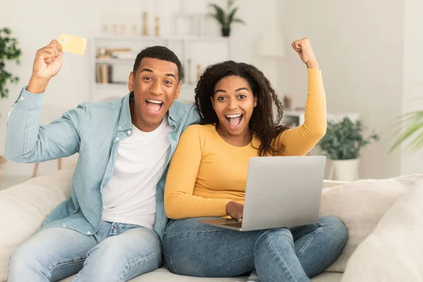 ラップトップで100万人のアフリカ系アメリカ人のカップル クレジットカードは勝利を収め リビングルームのインテリアで手で成功したジェスチャー 自宅での提供 良いニュースへの反応 販売とキャッシュバック — ストック写真