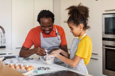 Mutfakta babamla yemek pişirirken güler yüzlü siyah kız, mutlu baba ve önlüklerini giyip evde yemek pişiren, pasta yaparken eğlenen, yakın çekim yapan genç kız.