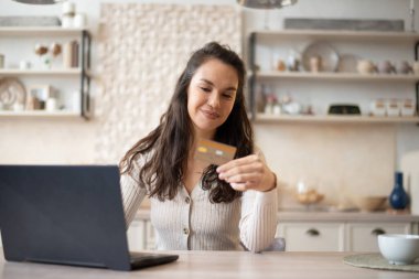 Bilgisayardan alışveriş yapan, kredi kartı kullanan, mutfaktaki masada oturan, online ödeme yapan beyaz bir kadın. İnternet bankacılığı ve ecommerce hizmeti kavramı