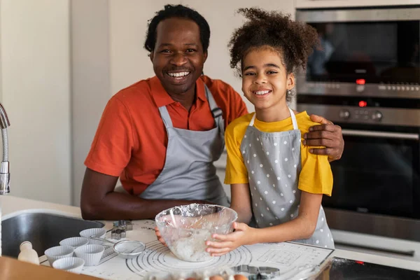 Happy Black Dad And Daughter Posing At Camera While Baking In Kitchen, Cheerful African American Family Father And Preteen Female Child Having Fun While Cooking Together At Home, Copy Space