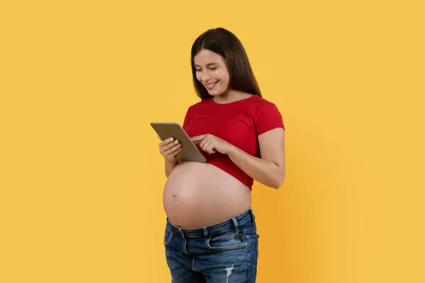 Usmívající Těhotná Žena Pomocí Digitální Tablety Zatímco Stojí Nad Žlutým — Stock fotografie