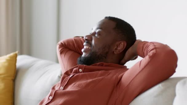 周末放松 年轻无忧无虑的非洲裔美国人的近照 躺在沙发上 手背着头 微笑着 跟踪镜头 慢动作 自由自在 — 图库视频影像