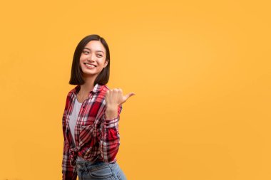 Şuna bir bak. Mutlu Asyalı kadın fotokopi odasına bakıyor ve işaret ediyor. Pozitif Koreli kadın reklam için boş alan gösteriyor. Sarı stüdyo arka planında poz veriyor.