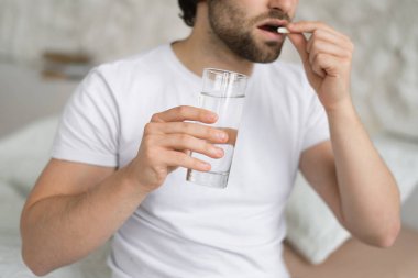 Üzgün, çaresiz, beyaz bir adam acıdan, hastalıktan muzdarip, haplar alıyor, bir bardak su tutuyor, yatak odasının iç kısmında yatıyor. Sağlık sorunları ve hastalıklar için antibiyotikler, ağrı kesiciler