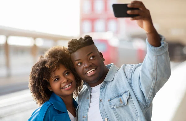 Happy Young Black Couple Taking Selfie On Smartphone At Railway Station, Cheerful African American Man And Woman Using Mobile Phone For Making Photos While Waiting Train On Platform, Closeup