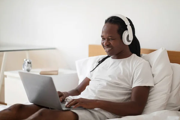 Black Man Wearing Wireless Headphones Using Laptop While Sitting Bed — Photo
