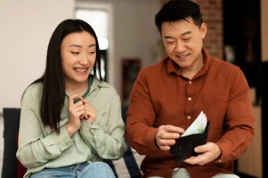 Zengin Asyalı olgun koca karısına para veriyor, evdeki kanepede oturuyor. Bir adam bayana euro banknotlarıyla ödeme yapıyor. Mali bolluk aile bütçesi kavramı