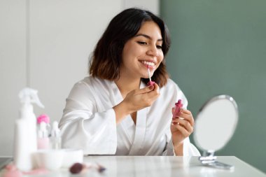 Ortadoğulu güzel bir kadın aynaya bakıyor, ruj sürüyor, evin içi boş. Çekici bir bayan güzel dudaklarıyla ilgileniyor, parlak dudak parlatıcısı sürüyor, makyaj yapıyor.