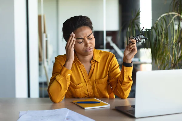Unhappy black female freelancer feeling tired of working on laptop, suffering from headache in office interior. Businesswoman having deadline stress during online job