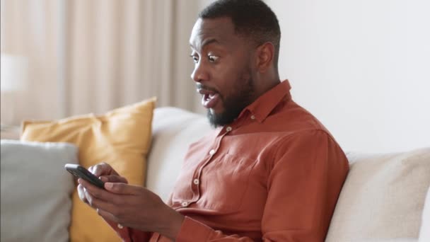 在线赌博和成功 用智能手机上网的兴奋的黑人年轻人的侧面肖像 获得了胜利的信息 在家里享受突如其来的胜利 慢动作 自由自在的空间 — 图库视频影像
