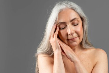 Olgun Avrupalı kadınların elleriyle yüzlerine dokunması, güzellik prosedürlerinin ve gri arka planda, stüdyoda izole edilmiş gençleşmenin tadını çıkarması. Güzellik, kaplıca, yaşlanma önleyici tedavi ve nemlendirme