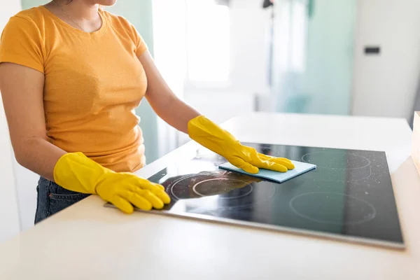 Housekeeping Concept. Young Woman In Rubber Gloves Cleaning Induction Cooktop With Rag, Unrecognizable Housewife Polishing Table Surface While Tidying Home, Enjoying Domestic Chores, Cropped