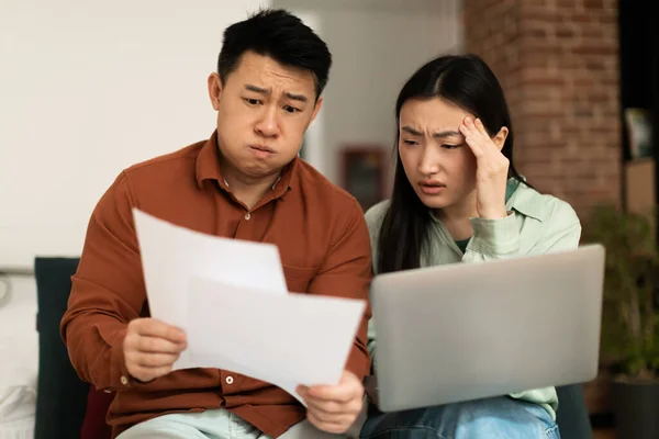 Stressed asian spouses checking financial papers, upset mature husband and young wife looking at loan documents, calculating family budget, suffering financial crisis