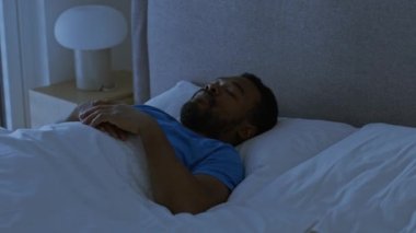 Gece uykusu kavramı. Genç, yorgun, Afro-Amerikalı, yatakta tek başına uyuyan, rahat yatak örtüleri, takip çekimi, yavaş çekim, serbest alan