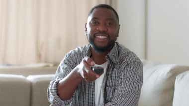 Komik televizyon içeriği. Genç, ilgilenen Afro-Amerikan bir adamın portresini kapatın. Uzaktan kumandayla TV 'de kanal değiştiriyor, yayın servisinin keyfini çıkarıyor, yavaş çekim, serbest alan.
