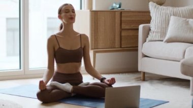 Zen ve yaşam dengesi kavramı. Genç, sakin bir bayan evde meditasyon yapıyor. Nilüfer pozisyonunda, tabletin önünde oturuyor. Sakinleştirici müzik, takip çekimi, yavaş çekim, serbest alan.