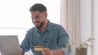 Çevrimiçi bankacılık servisi. Genç kaygısız Arap çalışanı internette ödeme yapıyor, web sitesine kredi kartı verileri ekliyor, evde dizüstü bilgisayarda çalışıyor, çekim takibi, yavaş çekim, serbest alan