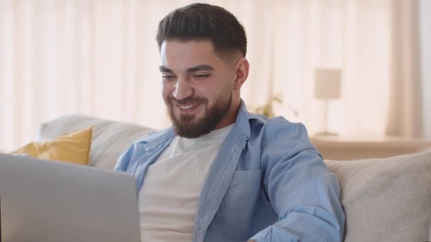 リラックスしたレジャー 若いですハンサムな正のアラブ人男性を見てデジタルテレビやノートパソコンでニュースを読む 自宅で休んで 撮影を追跡 スローモーション フリースペース — ストック動画