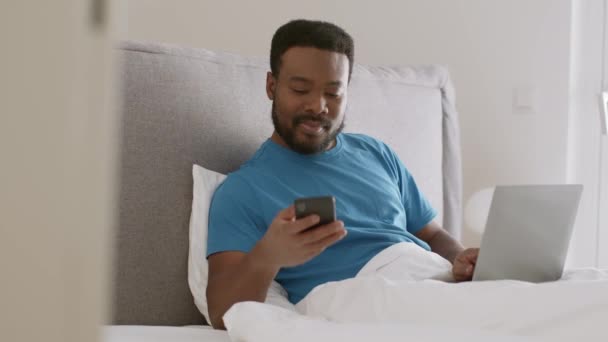 Ung Afrikansk Amerikan Som Arbetar Laptop Sängen Svarar Telefon Och — Stockvideo