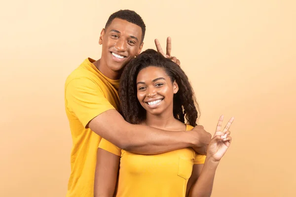 Joyful Young Black Man Hugging His Girlfriend Making Horns Fingers — Stockfoto