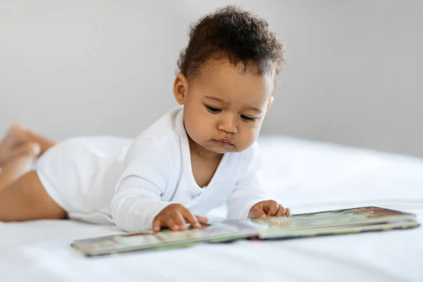 Adorable Black Baby Looking Pictures Book While Relaxing Bed Home —  Fotos de Stock