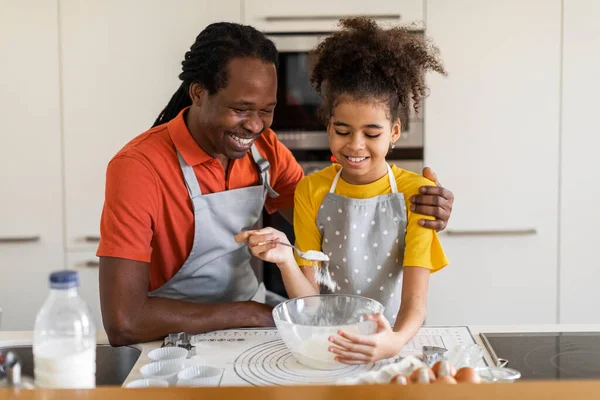 Home Bakers. Cheerful Black Dad And Preteen Daughter Baking Together In Kitchen, Happy African American Father And Female Child Preparing Dough For Pastry, Girl Adding Flour To Bowl, Free Space