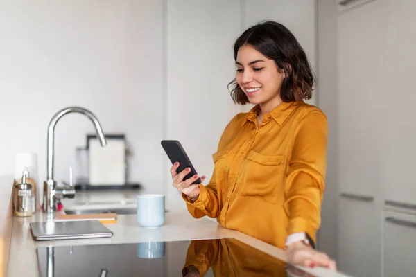 自宅のキッチンでスマートフォンでオンラインショッピングを作る幸せな若いアラブ人女性 インターネット購入のための携帯電話で現代のアプリを使用して笑顔ミレニアル中東女性 コピースペース — ストック写真