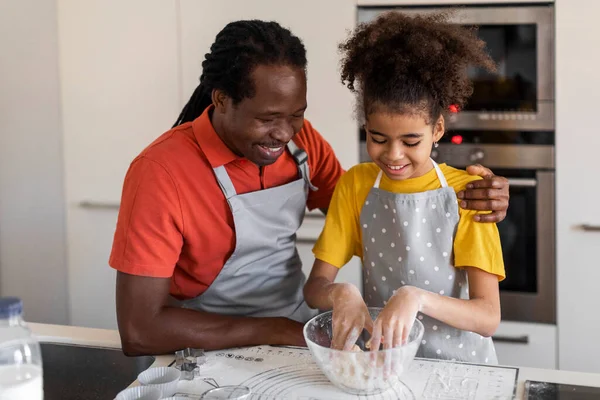 Black girl and her father kneading dough while baking in kitchen, happy african american man and his female child cooking at home, enjoying making homemade pastry, closeup shot with free space