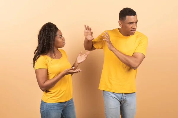 African american couple arguing, angry displeased black woman yelling at annoyed boyfriend who ignoring her, standing over yellow studio background. Relationship problem concept