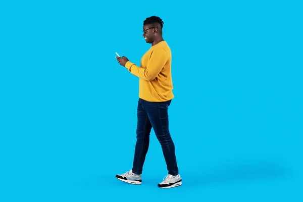 Young Black Man Walking Smartphone Hands Blue Studio Background Happy —  Fotos de Stock