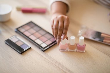 Cropped of female blogger hands with nice manicure showing various beauty products, unrecognizable dark-skinned woman testing different makeup essentials, high angle view shot