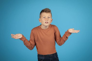 I Dont Know. Doubtful Preteen Boy Shrugging Shoulders And Spreading Arms, Portrait Of Doubtful Kid Looking At Camera, Unsure Male Child Standing Isolated Over Blue Studio Background, Copy Space