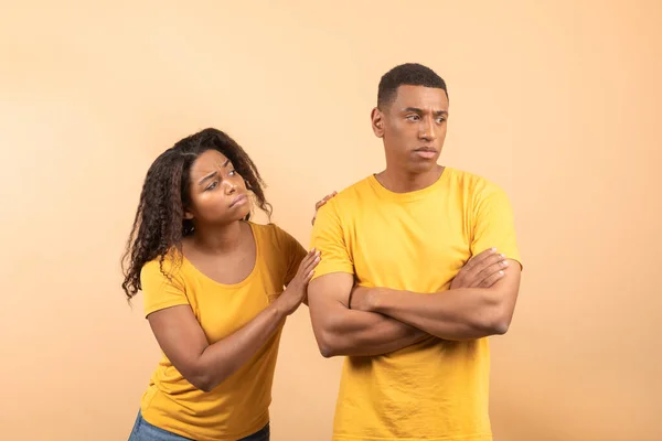 African american lady asking forgiveness after saying wrong words to beloved black boyfriend, standing over yellow background, studio shot