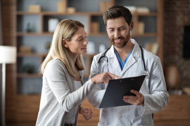 Therapist Man And Female Patient Discussing Medical Treatment At Meeting In Office, Handsome Male Doctor In Uniform Holding Clipboard And Explaining Medicine Prescription To Smiling Woman