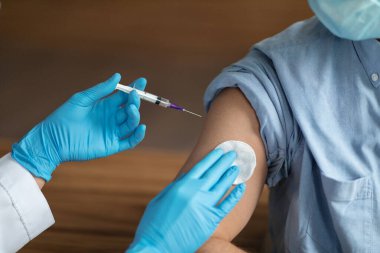 Unrecognizable Nurse Holding Syringe, Making Vaccine Shot To Shoulder Of Male Patient, Young Man In Medical Mask Getting Vaccinated Against Covid-19 In Clinic, Cropped Image, Closeup