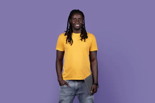 ポジティブなクールなハンサムな若いですアフリカ系アメリカ人長いです髪男でカジュアル開催現代のラップトップ上の紫のスタジオの背景 黒男フリーランサーポーズとともに現代のコンピュータ コピースペース — ストック写真