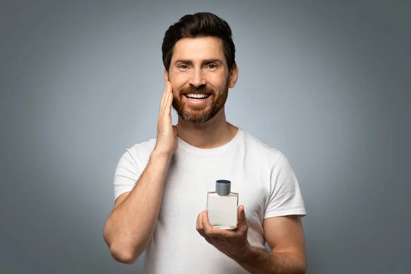 仪容整洁与人的概念 快乐英俊的高加索男人在胡子上涂上香水 在灰色的工作室背景上摆出姿势 对着相机微笑 — 图库照片