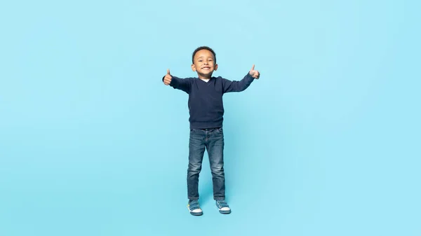 真诚的认可 全长的肖像画 描绘了一个无忧无虑的小非洲裔美国男孩微笑着 竖起大拇指 站在蓝色工作室的背景上 自由自在的空间 — 图库照片