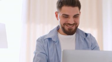 Happy freelance work. Close up portrait of young middle eastern guy digital nomad typing on laptop computer, enjoying his remote work at home office, tracking shot, slow motion, free space