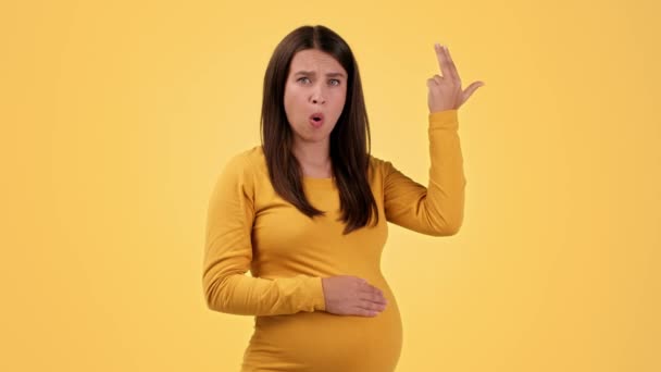 妊娠中のホルモンの変動 若い感情的な妊娠中の女性のスタジオの肖像画は 彼女の腹を愛撫 動揺感 オレンジの背景 スローモーション — ストック動画