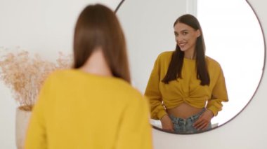 Natural beauty concept. Over shoulder portrait of young beautiful lady looking at mirror and smiling, anticipating her appearance, smiling to reflection, tracking shot, slow motion, free space